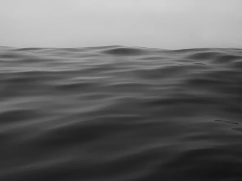 Inceville I — black-and-white photograph shot from water level, dark undulating ocean surface filling the frame with a sliver of hazy sky. Medium format film by Alex Hoerner.