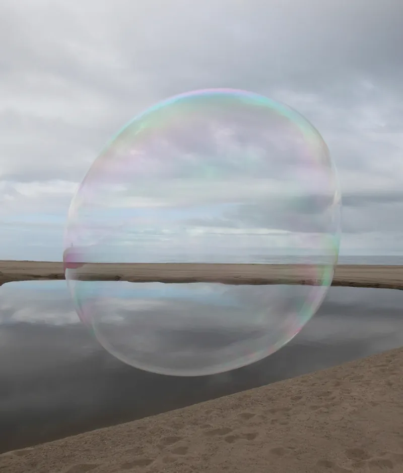 Surface Tension I — large iridescent soap bubble floating over a beach tidal pool with sand and ocean horizon, Santa Monica shoreline. Medium format film by Alex Hoerner.