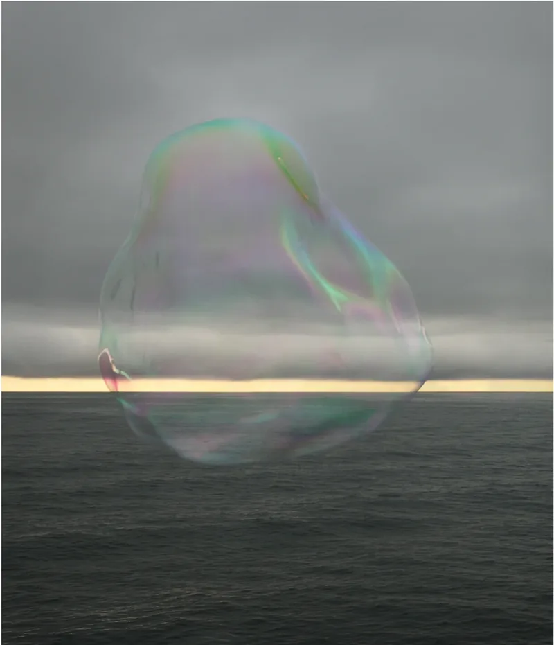 Surface Tension II — distorted iridescent soap bubble collapsing against a dramatic dark sky and sea with a thin golden strip of light at the horizon. Medium format film by Alex Hoerner.