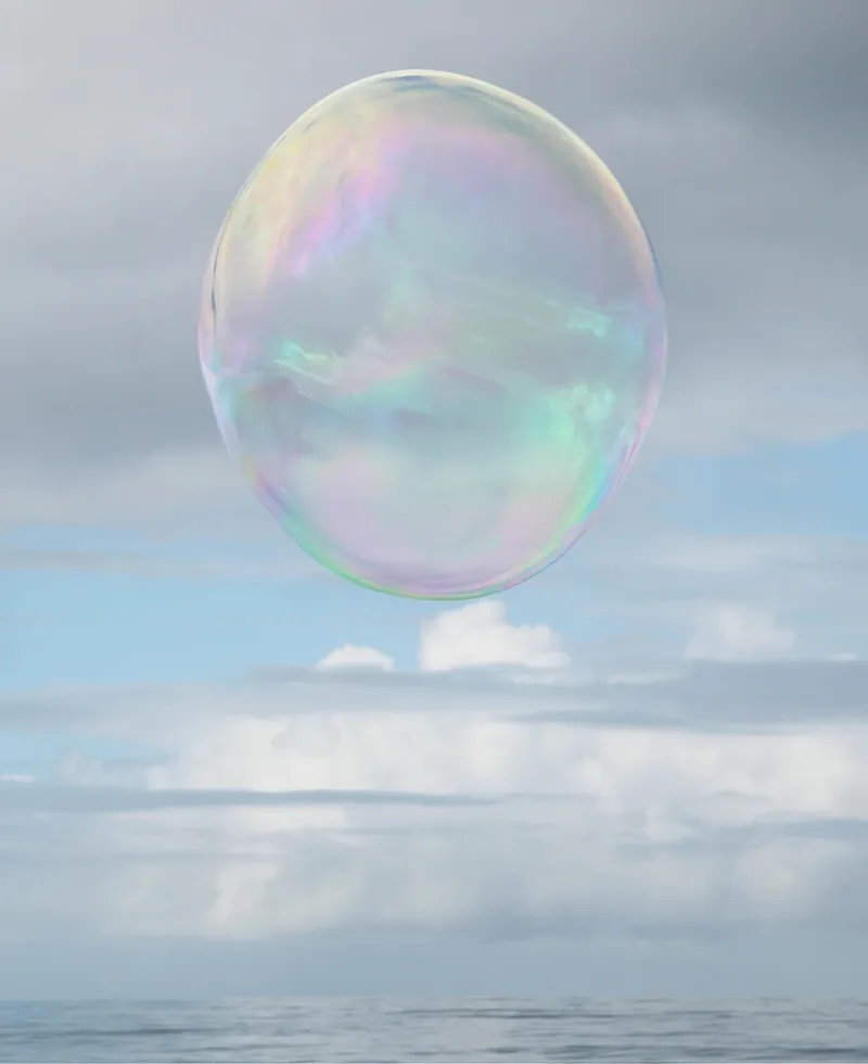 Surface Tension IV — near-perfect iridescent soap bubble floating high above the Pacific Ocean against a blue sky with scattered clouds. Medium format film by Alex Hoerner.
