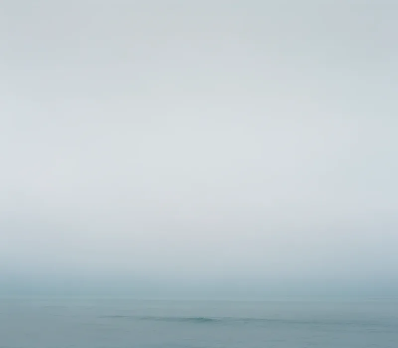 Untitled I — minimal June Gloom seascape, pale gray-green sky merging with calm ocean and a single small wave, Santa Monica Bay. Medium format film by Alex Hoerner.